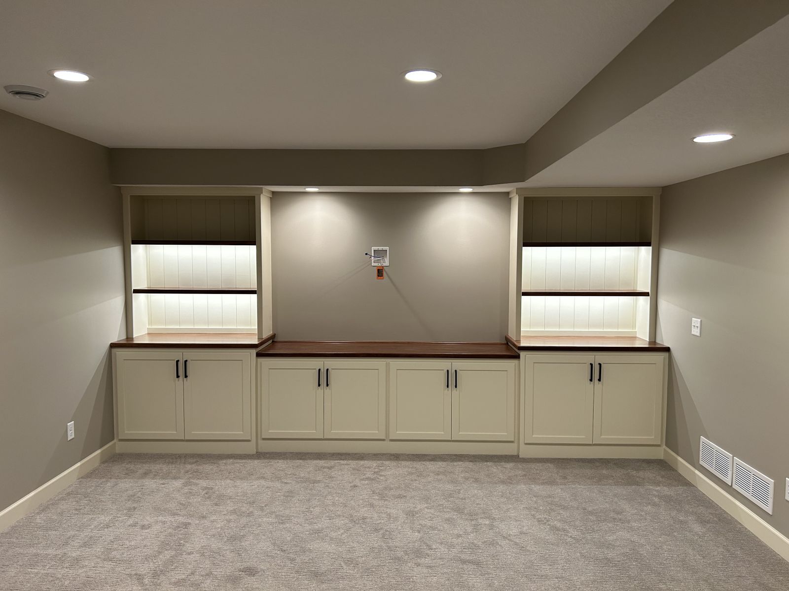 Bright finished basement room with recessed lights and illuminated built-in storage