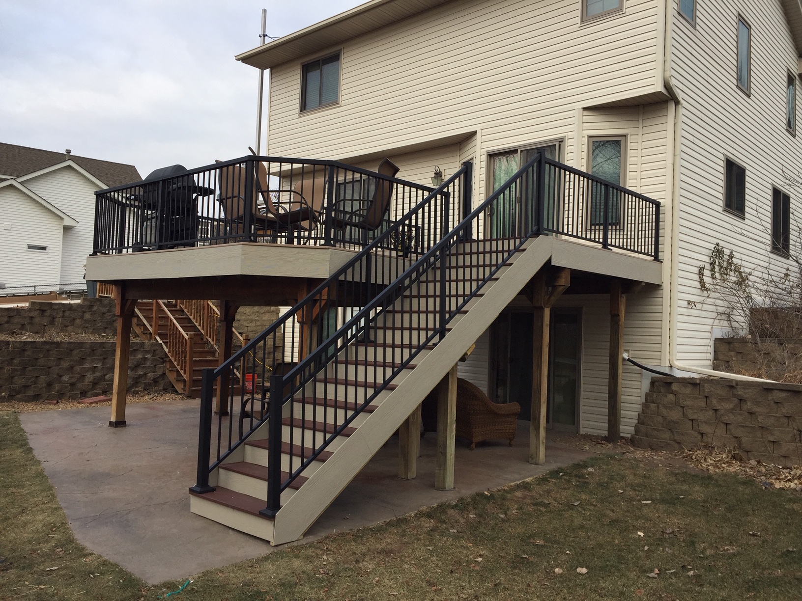 Raised deck with black railings, broad stairs and usable patio space below