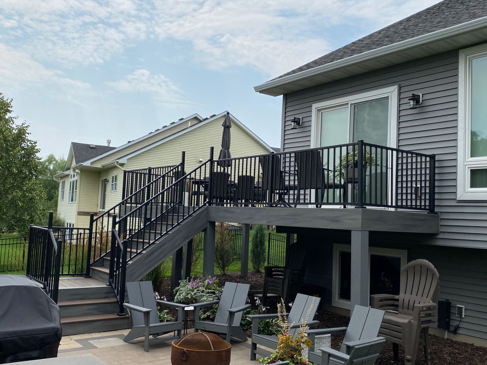 Elevated gray backyard deck with black railings and stairs beside a gray-sided home