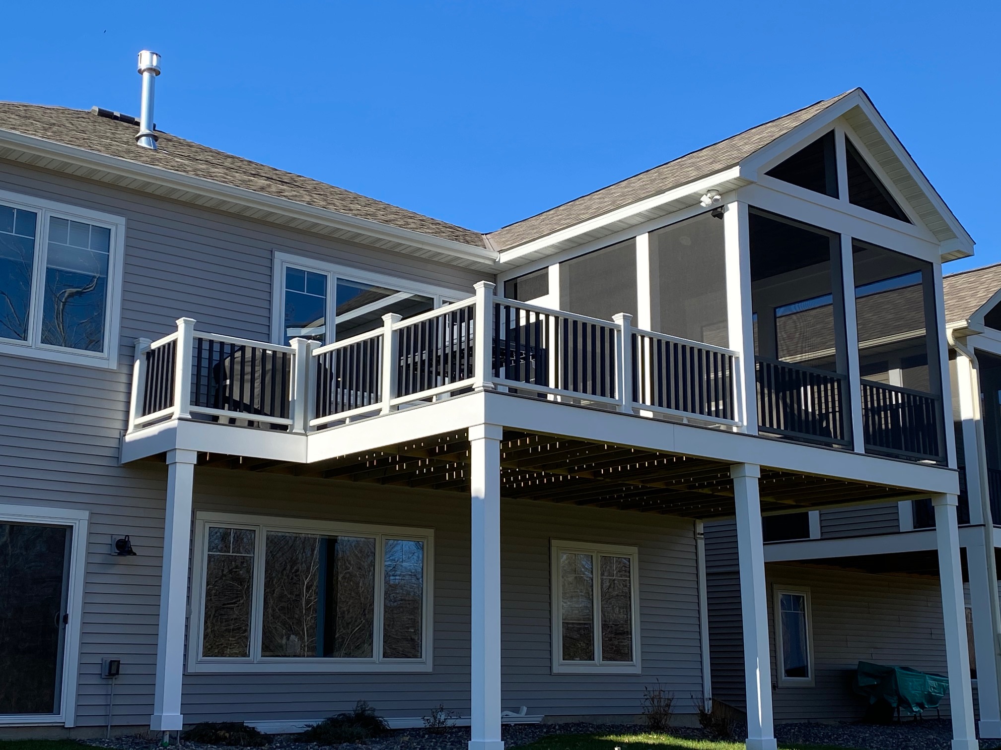 Elevated screened porch with white posts, dark railings and an adjoining outdoor platform